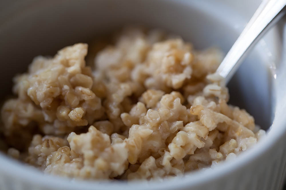 Cooked steel cut oatmeal in white bowl close up