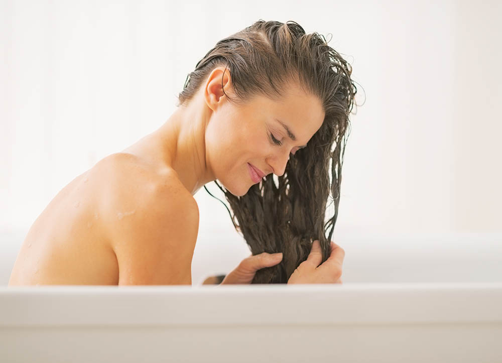 Happy young woman washing hair in bathtub