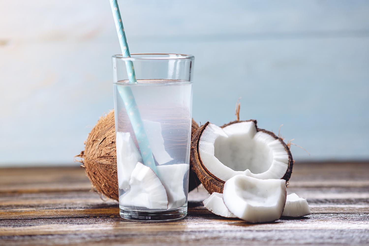 Coconut water in the composition with an open coconut with white flesh on a wooden background. Organic healthy dietary product widely used in cosmetology and Spa