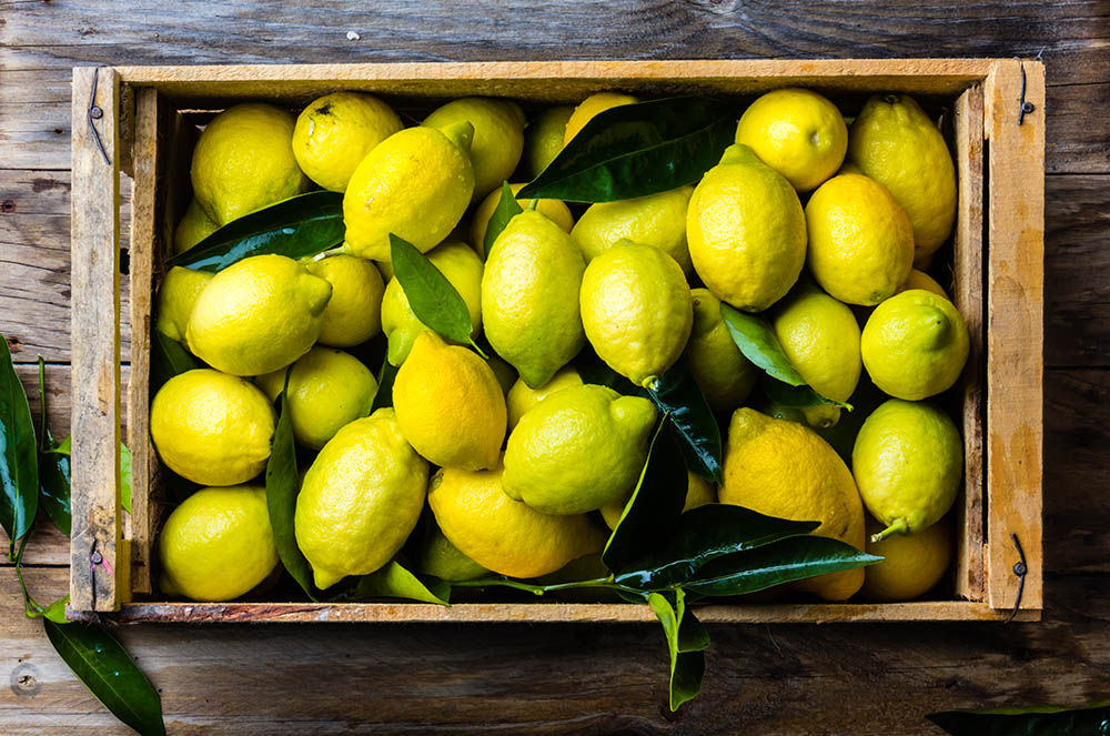 Fresh lemon with leaves. Lemon tree. Box of yellow lemons with fresh lemon tree leaves on wooden background. Top view