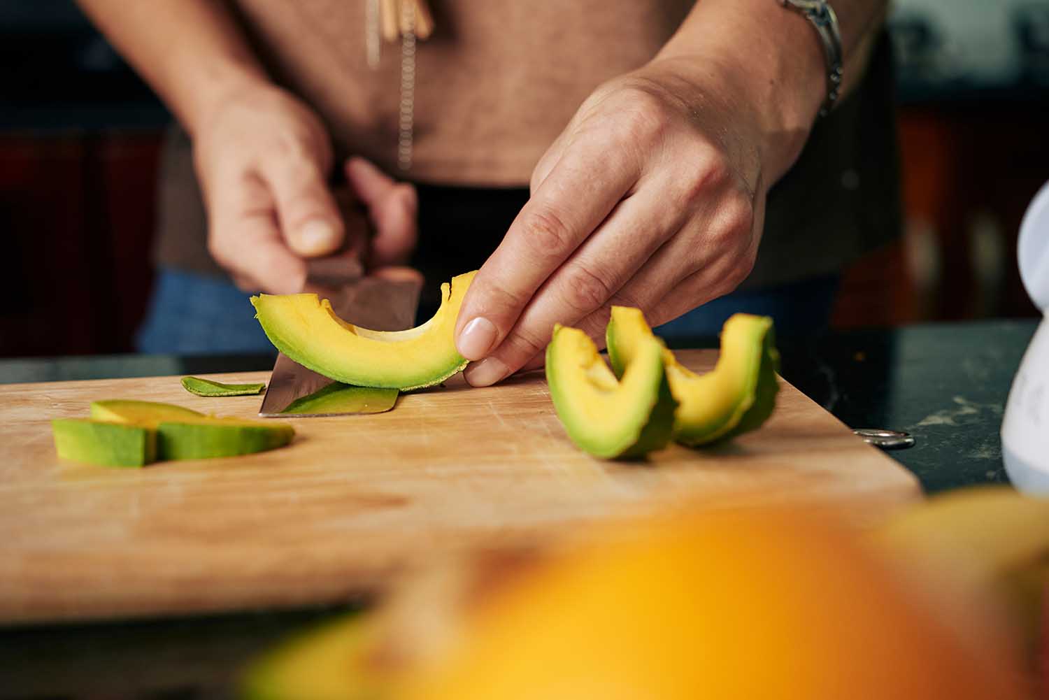 Hands peeling cut avocado slices on wooden board