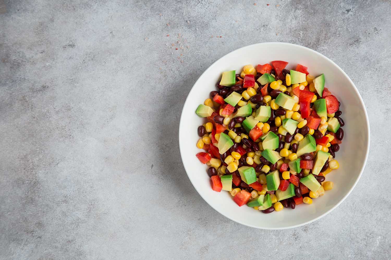 Avocado, black  bean, corn and bell pepper salad in white bowl. Top view, copy space