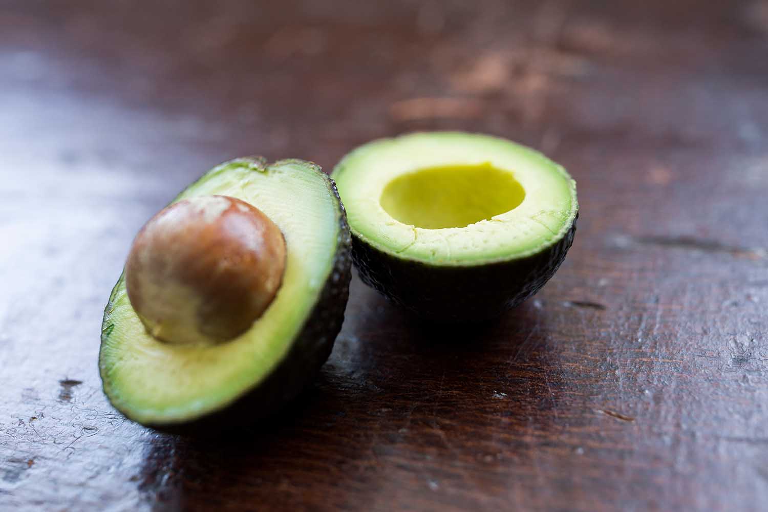 A sliced in half, fresh, green avocado with the pit inside on a vintage brown wooden table.