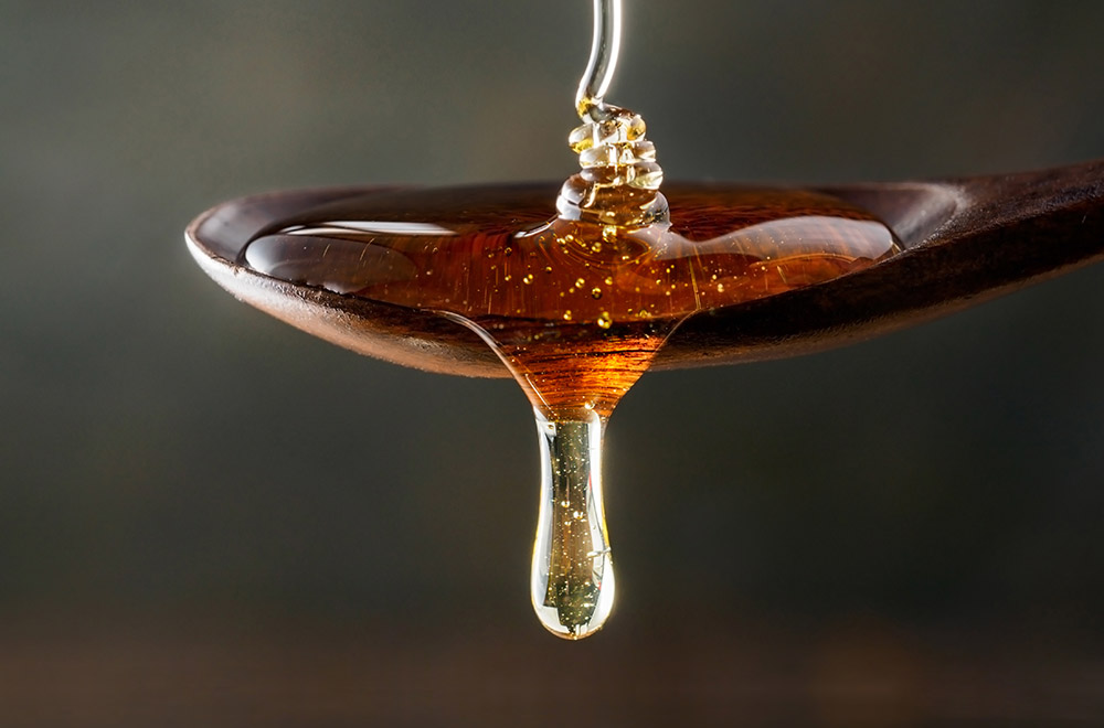 Honey pouring on wooden spoon and dripping from spoon. Dark background. Extreme close up