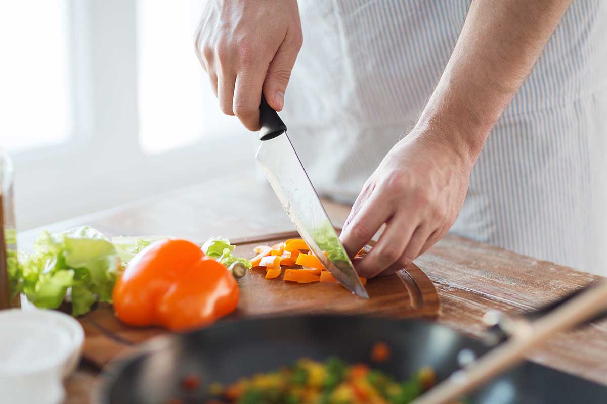 cooking, food and home concept - close up of male hand cutting pepper on cutting board at home