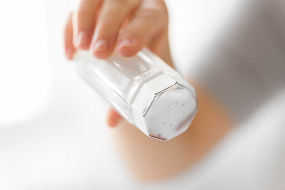 seasoning, culinary and unhealthy eating concept - close up of hand holding salt cellar