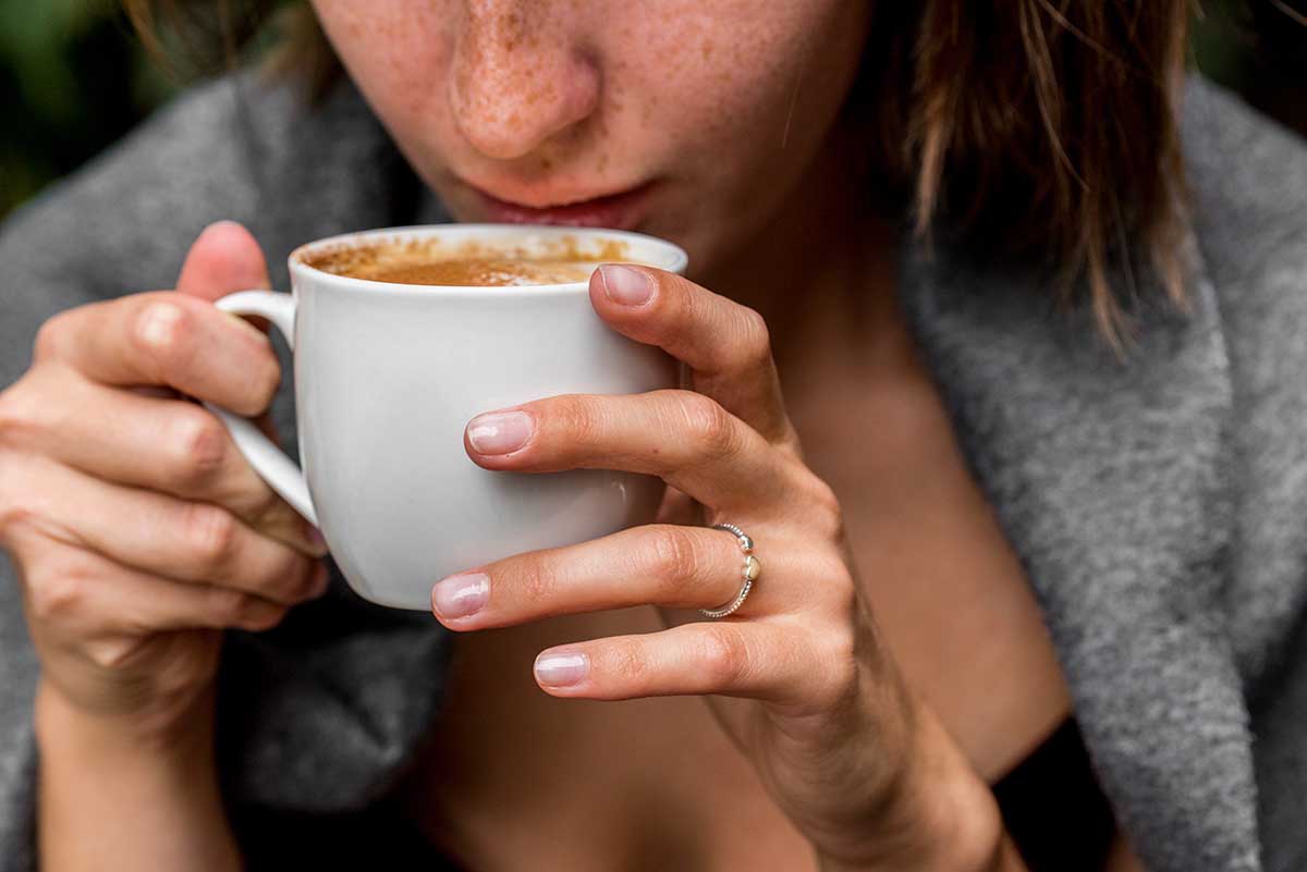 Pretty girl wrapped in blanket drinks coffee