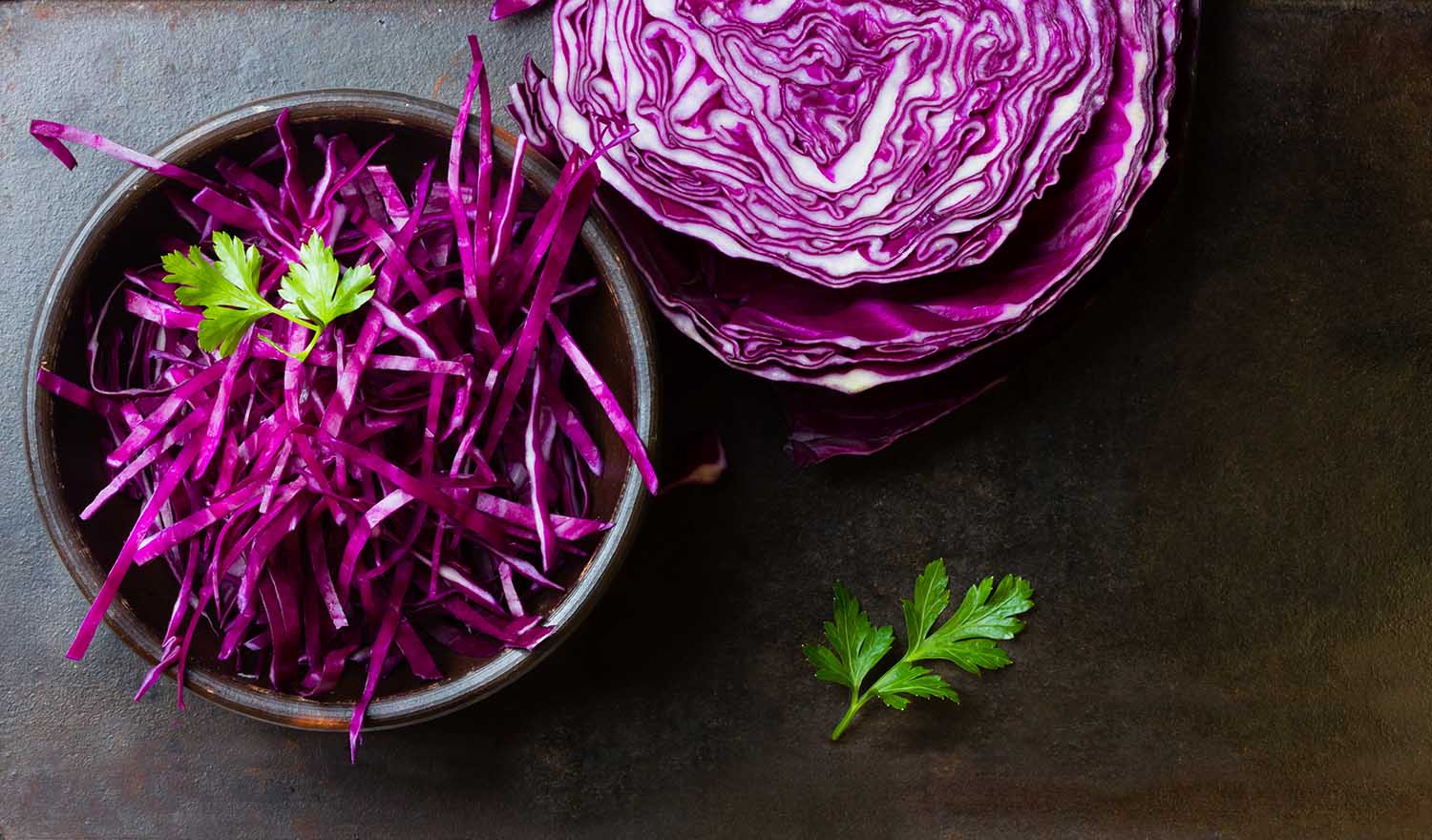 Shredded red cabbage in clay bowl on black background. Vegetarian healthy food. Top view