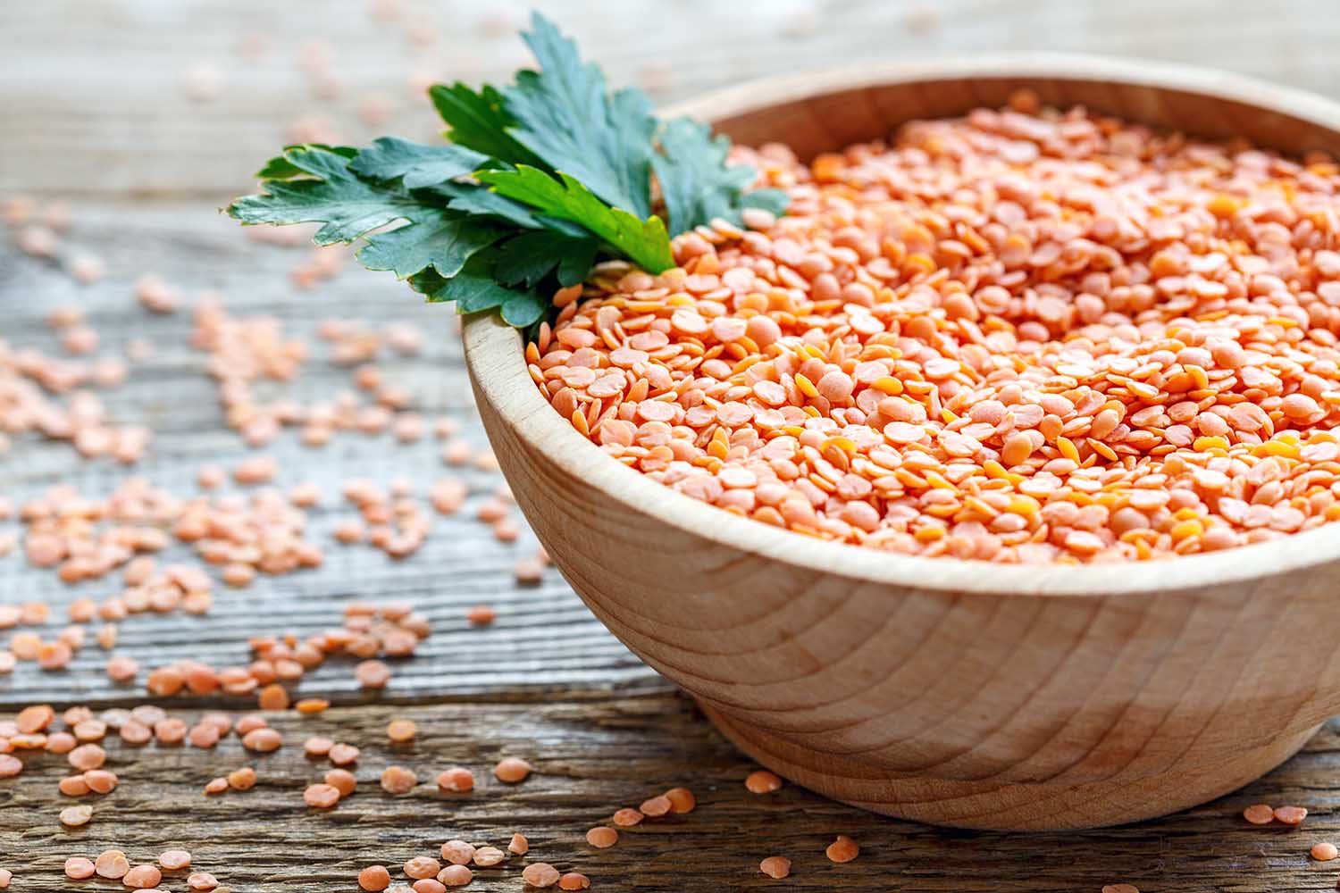 Heap of red lentils and parsley in a bowl on old wooden table.