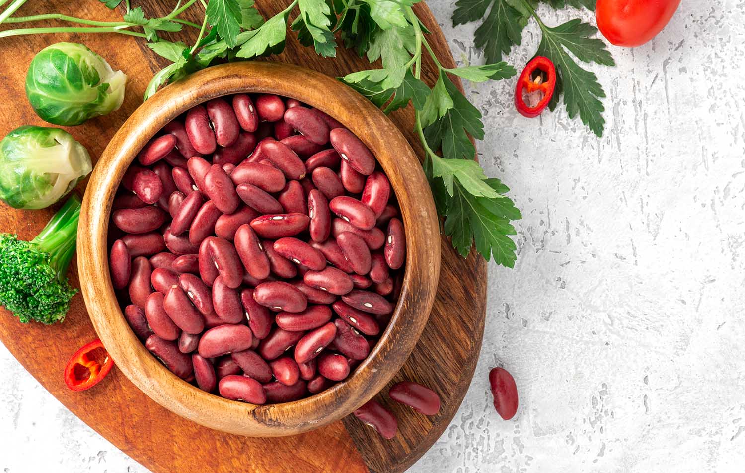 Uncooked dry red beans in a wooden bowl and vegetables on concrete background top view.