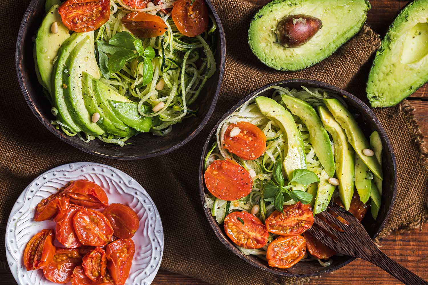Healthy salad with zoodles zucchini noodles, oven roasted tomatoes and avocado. The salad is seen from above, and it is served in recycled environmentally friendly coconut bowls.
