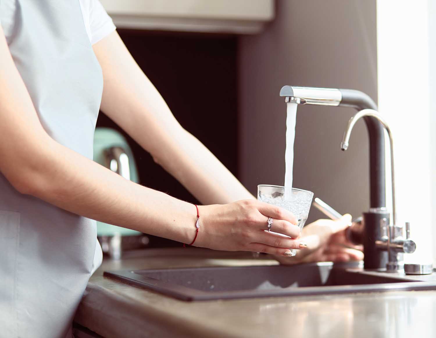 Human hand holding glass pouring fresh drink water at kitchen faucet