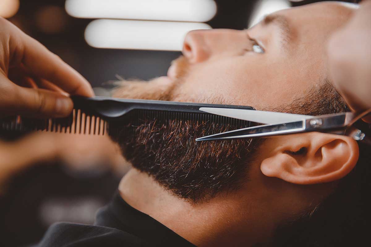 Close-up of barber shearing beard to man in barbershop