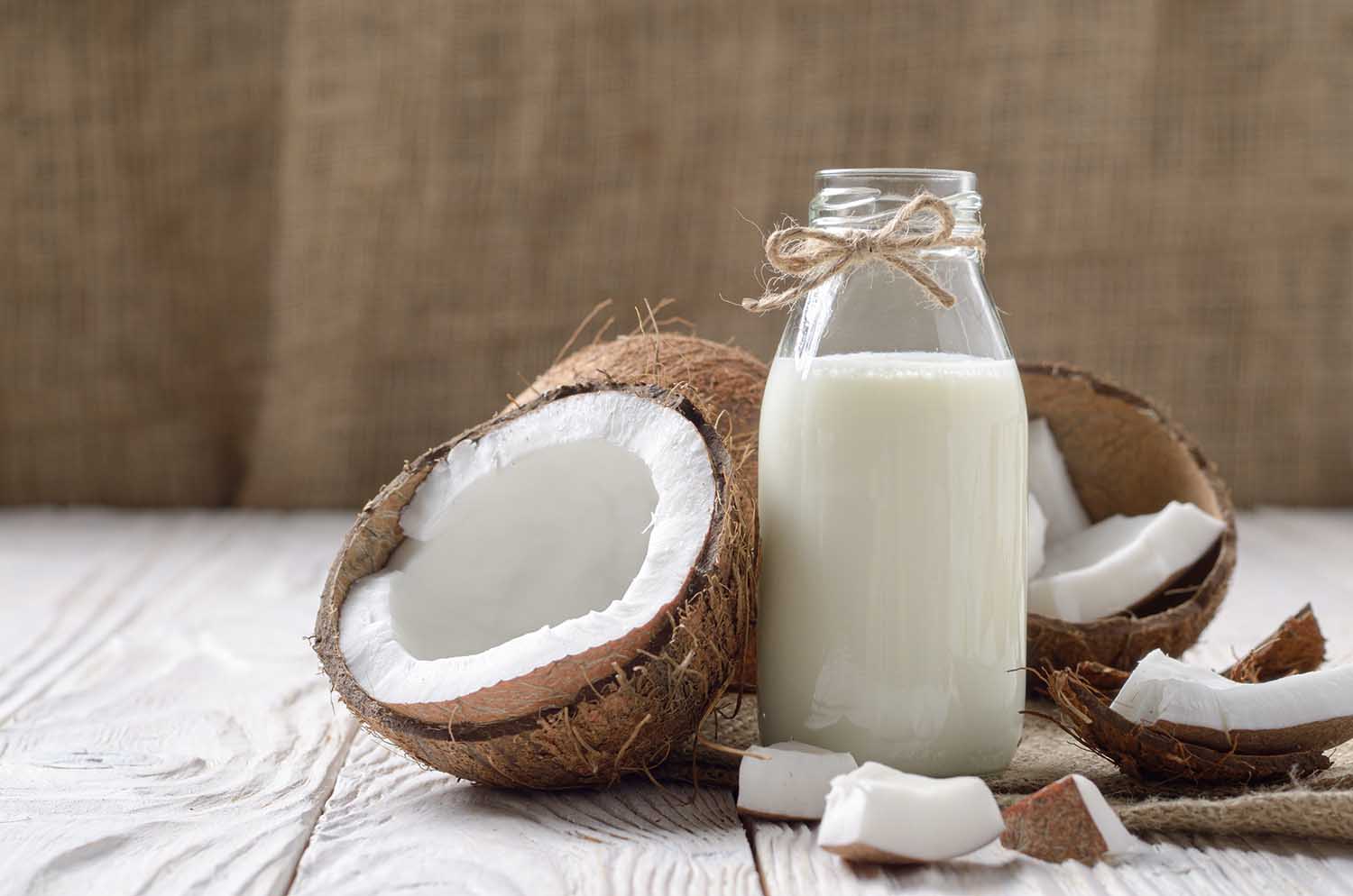 Glass bottle of milk or yogurt on hemp napkin on white wooden table with coconut aside