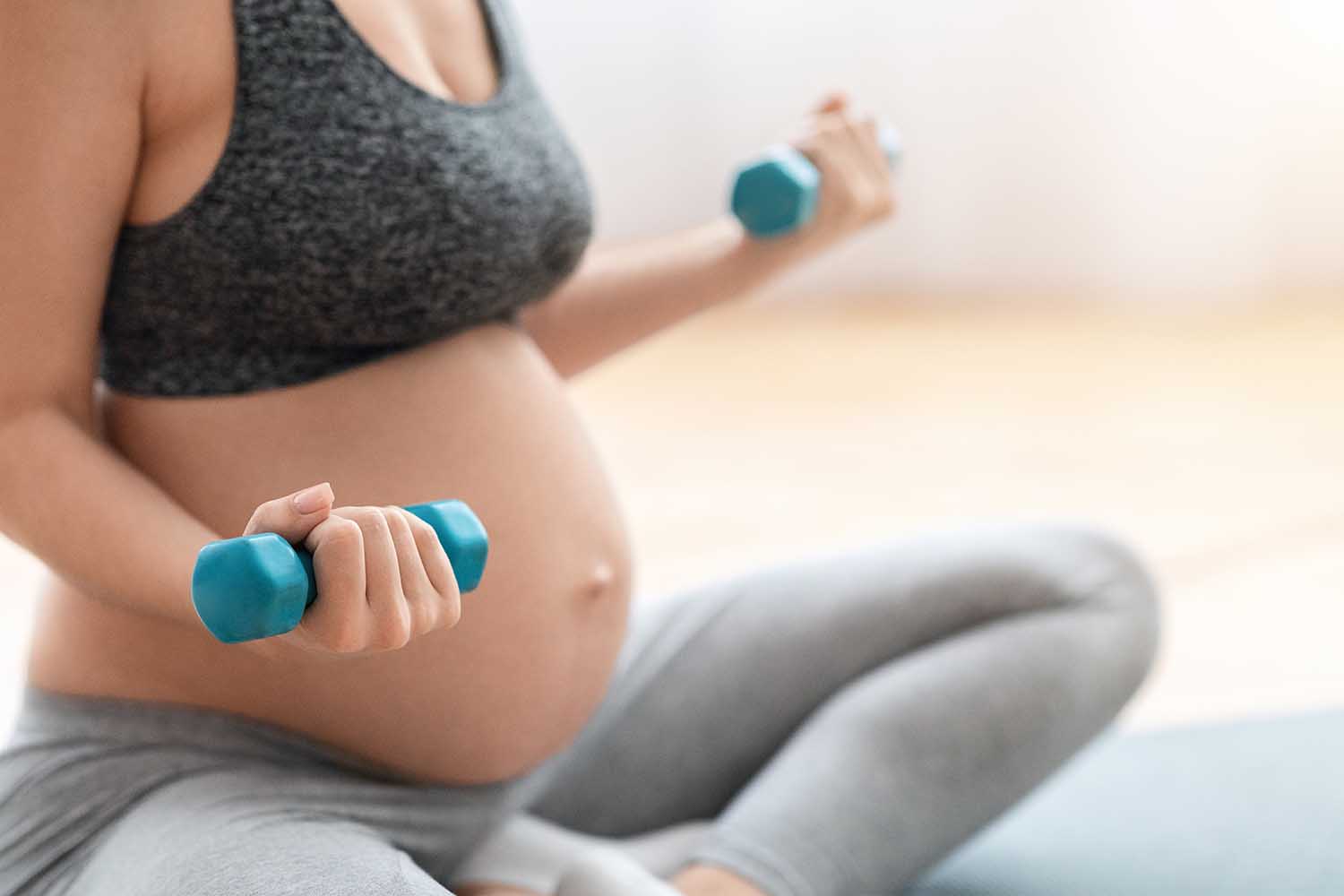 Cropped Shot Of Unrecognizable Pregnant Woman Training With Dumbbells At Home, Expectant Lady In Sportswear Exercising On Fitness Mat In Living Room, Closeup Image With Free Space