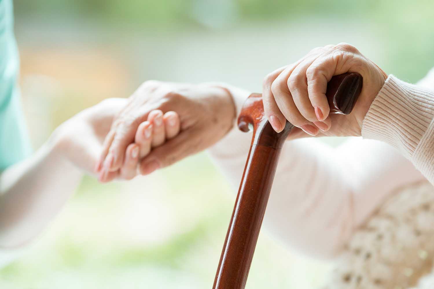 Elder person using wooden walking cane during rehabilitation in friendly hospital