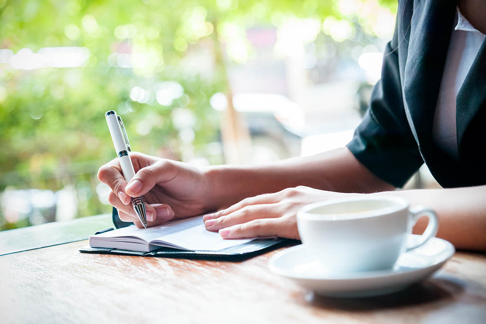 close up of woman writing journal and cup of coffee
