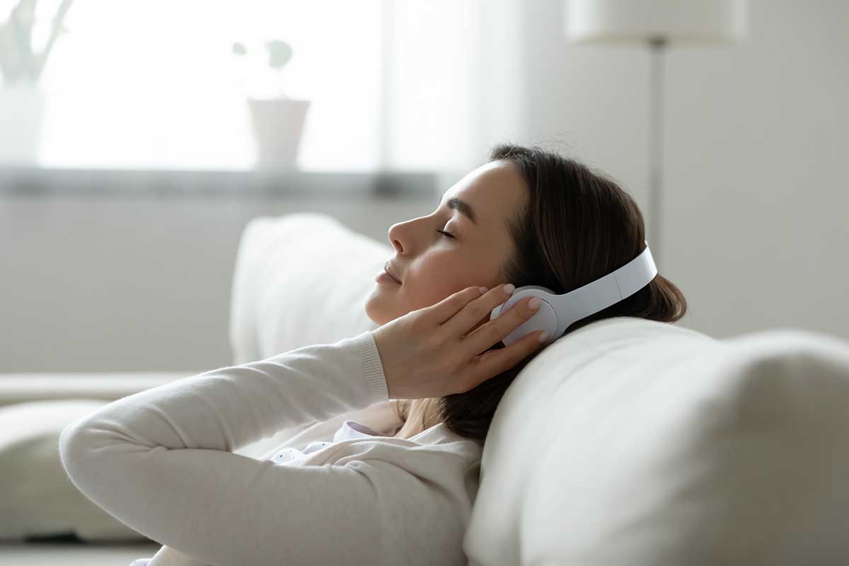 Calm female resting leaned on comfy couch in living room spend free time at home closed eyes enjoy music listening favourite song through wireless modern headphones. Pastime weekend relaxation concept