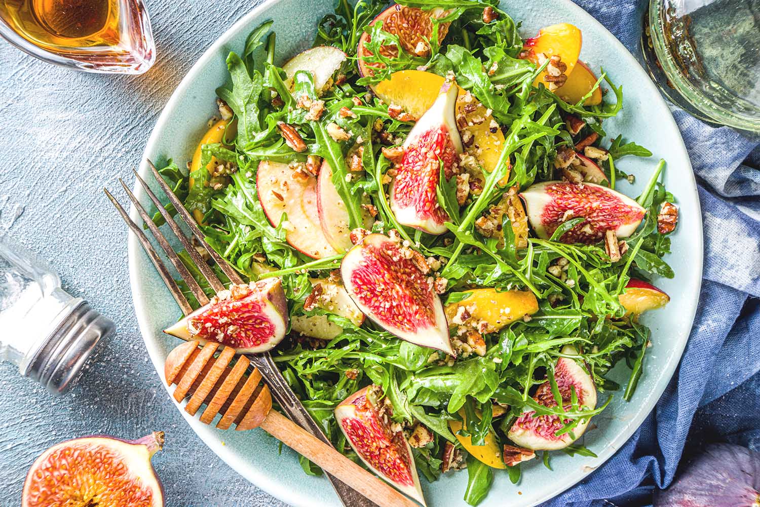 Autumn fig and arugula salad recipe. Whole vegan paleo fruit and vegetable fall salad idea. Homemade salad bowl with figs, arugula, peach and apple slices, nuts and honey.