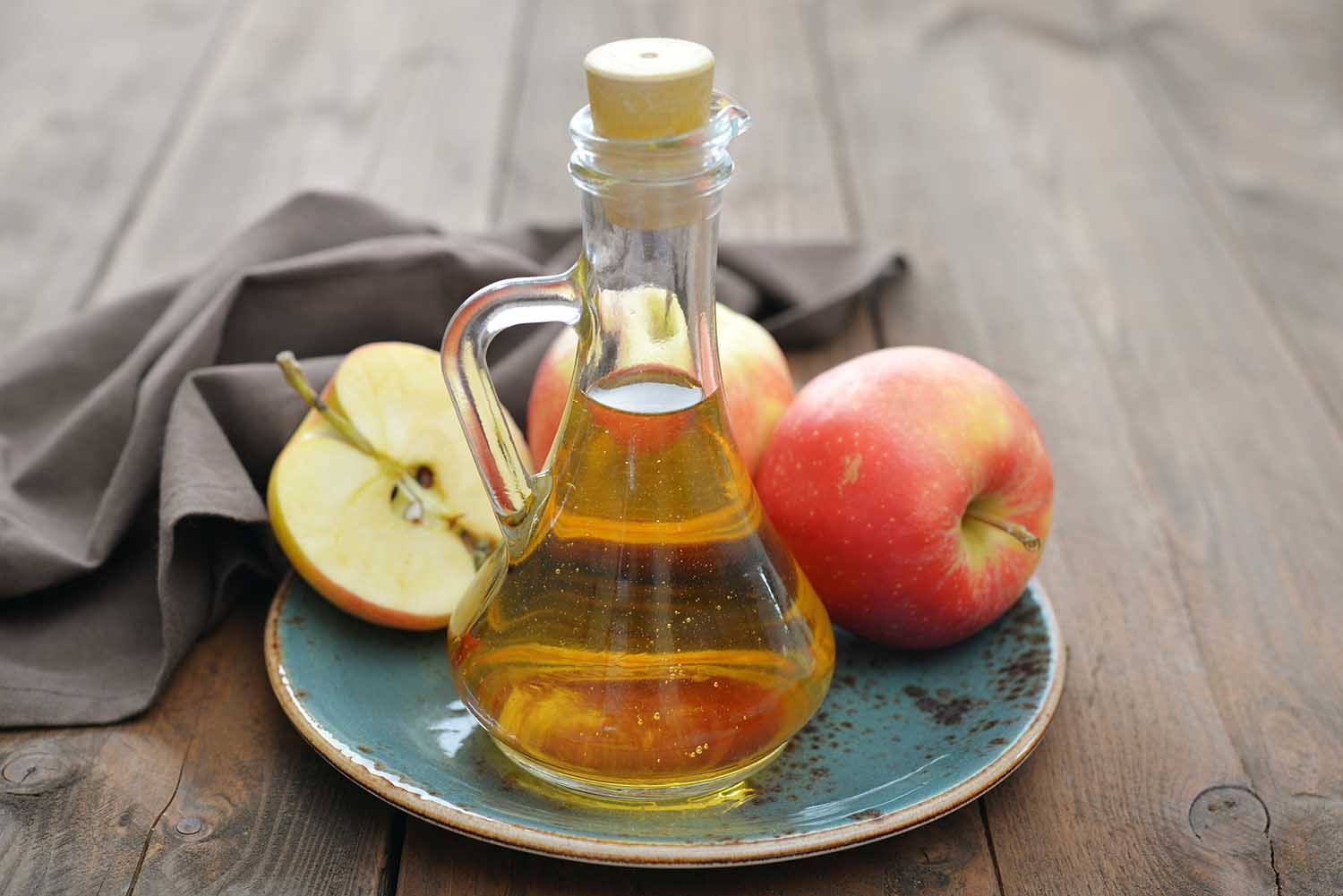 Apple cider vinegar in glass bottle and fresh apples on wooden background