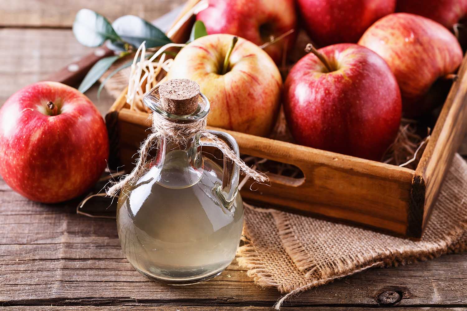 Bottle of unfiltered apple cider vinegar and apples in a wooden box over rustic background close up