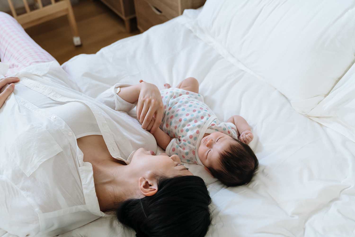 high angle view korean mother lying on bed with her young child. asian woman face to her baby daughter just put her kid to bed by singing gently to her.