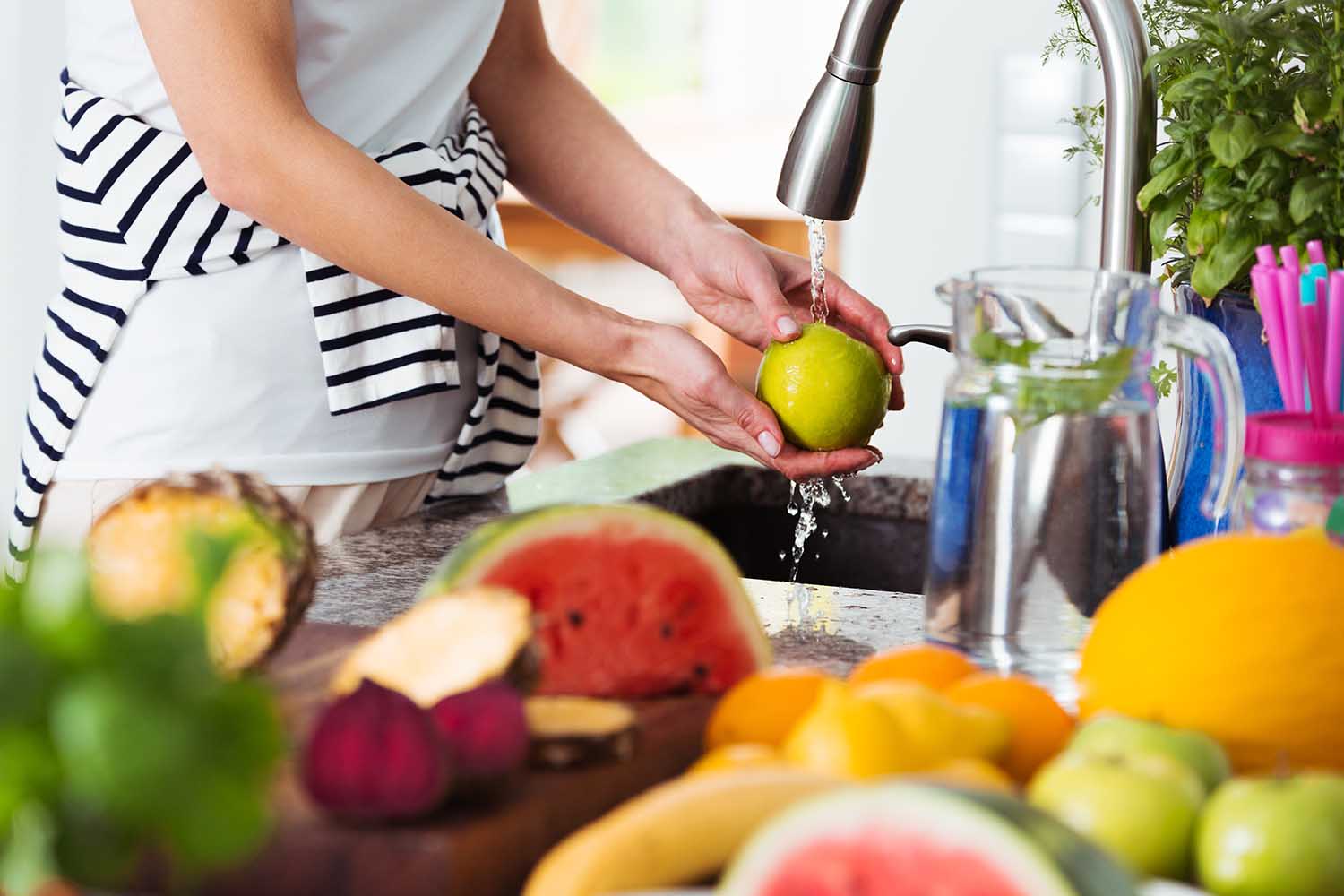 Healthy woman washing an apple above kitchen sink while preparing fresh breakfast with fruit