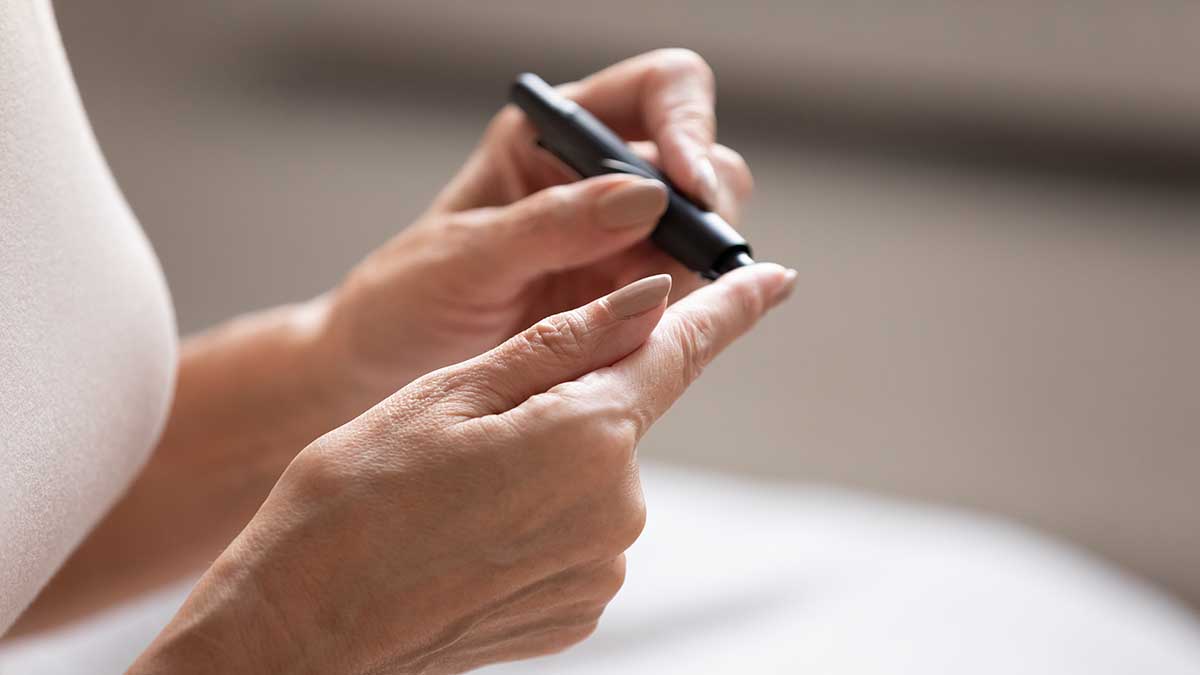 Close up older retired female hands with lancet pen on finger. Mature woman measuring sugar range or glucose level in blood herself in morning at home. Diabetes routine, healthcare domestic concept.