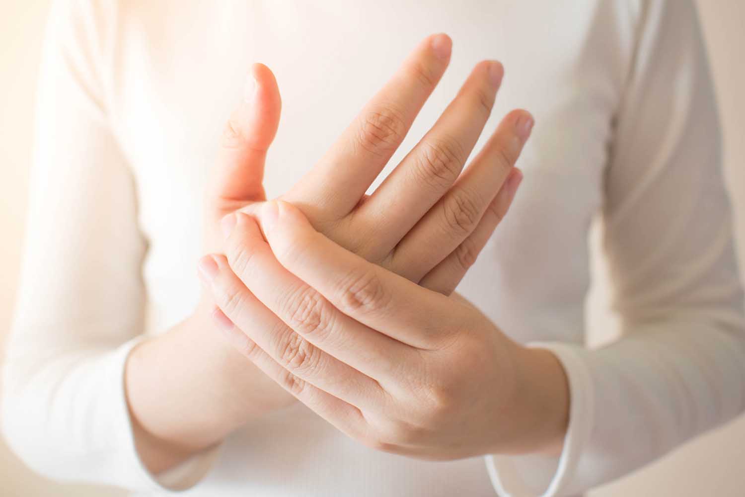 Young female in white t-shirt suffering from pain in hands and massaging her painful hands. Causes of hurt include carpal tunnel syndrome, fractures, arthritis or trigger finger. Health care concept.