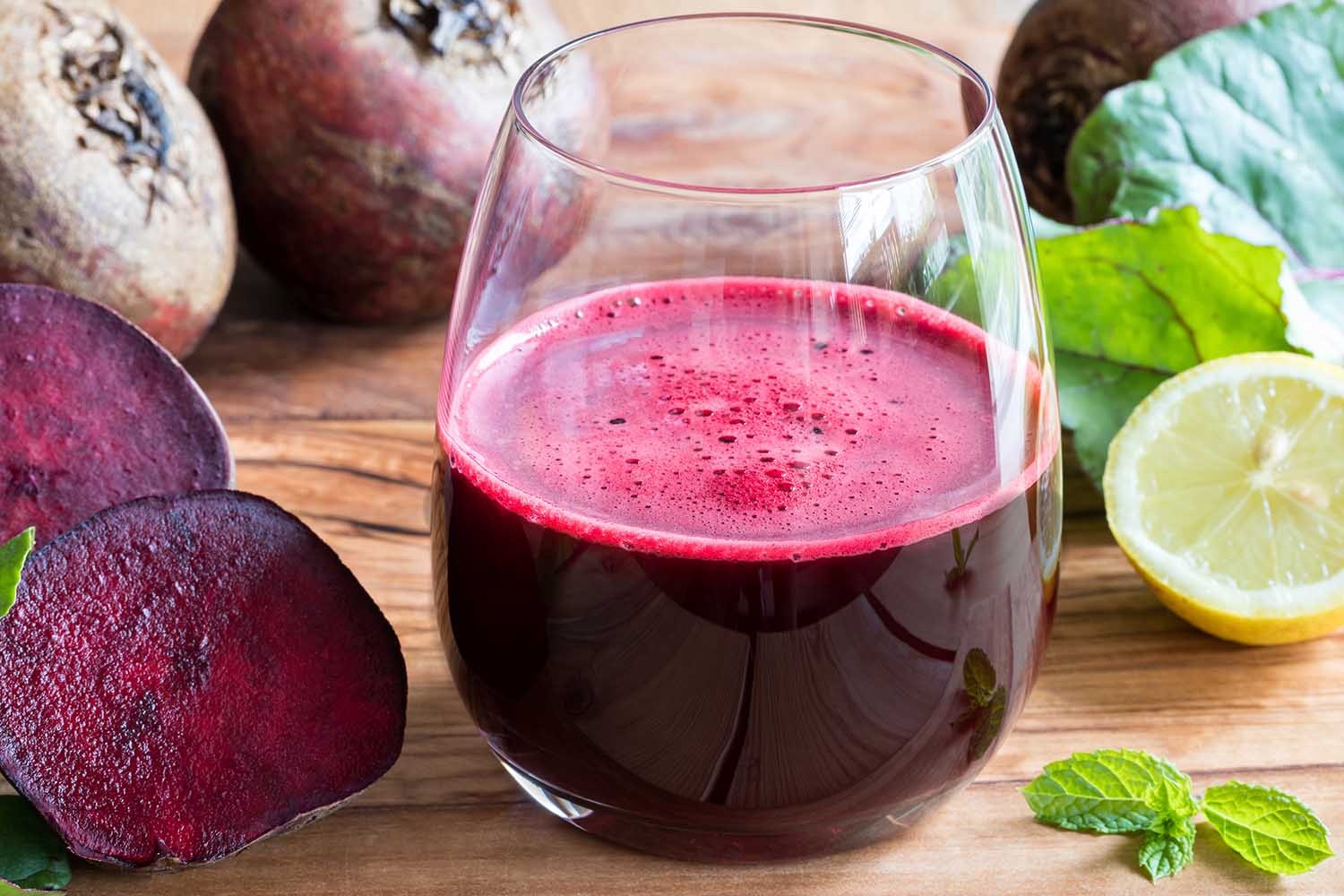 Red beet juice in a glass on a wooden background with lemon and beet greens