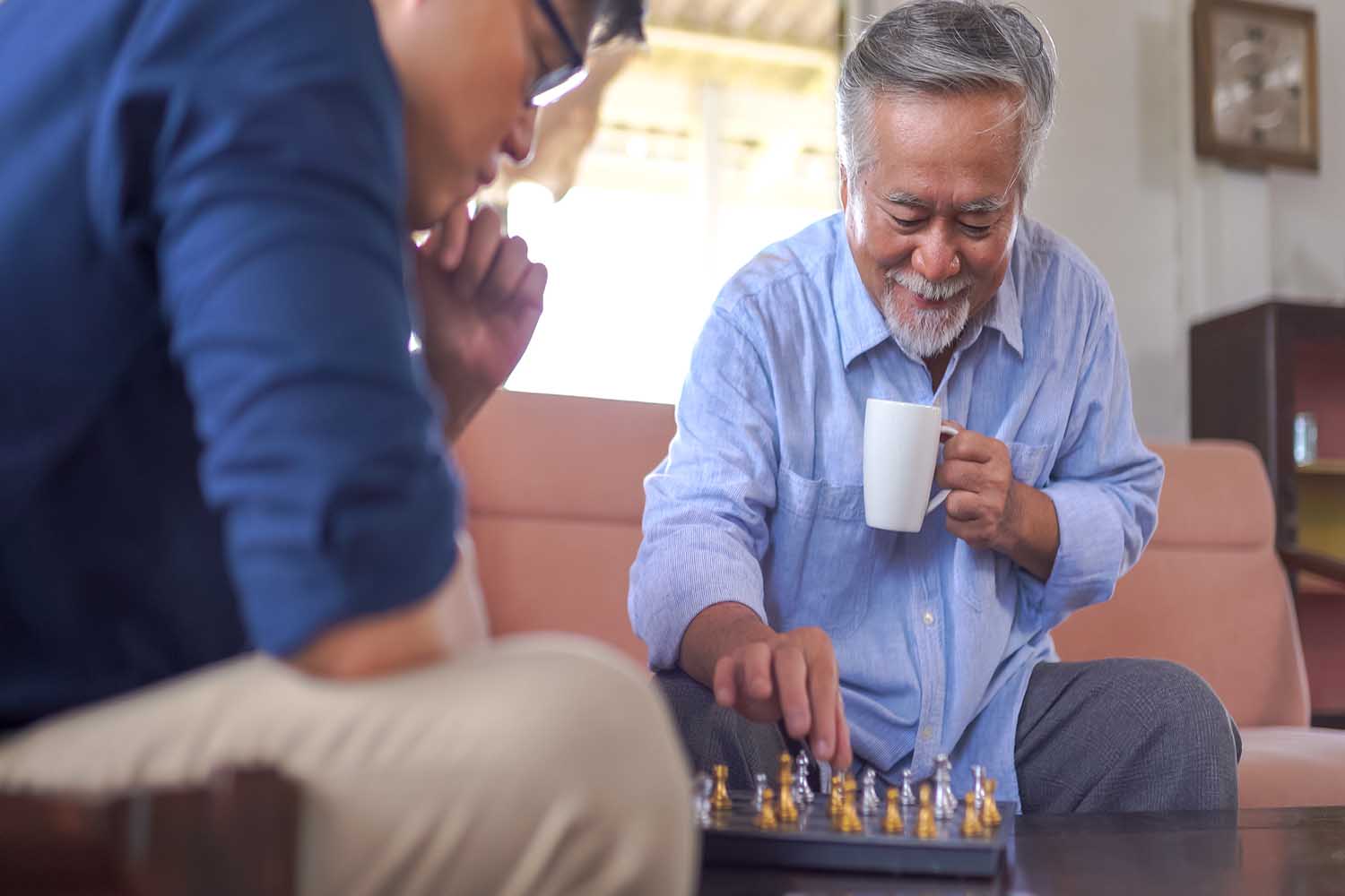 Asian Senior man playing chess with son at home