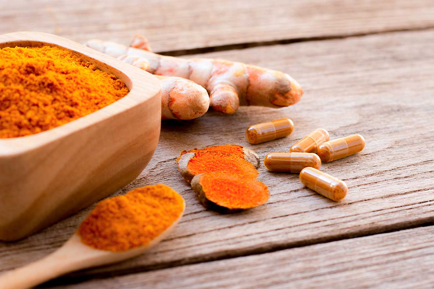 Turmeric ( curcumin, Curcuma longa Linn) powder capsules and tumeric ground in wooden bowl and spoon isolated on wood table background.