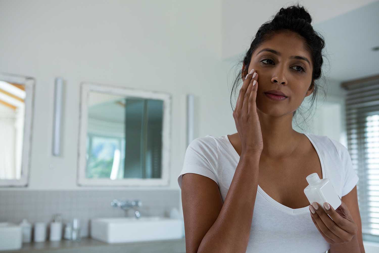 Close up of young woman applying lotion in bathroom at home