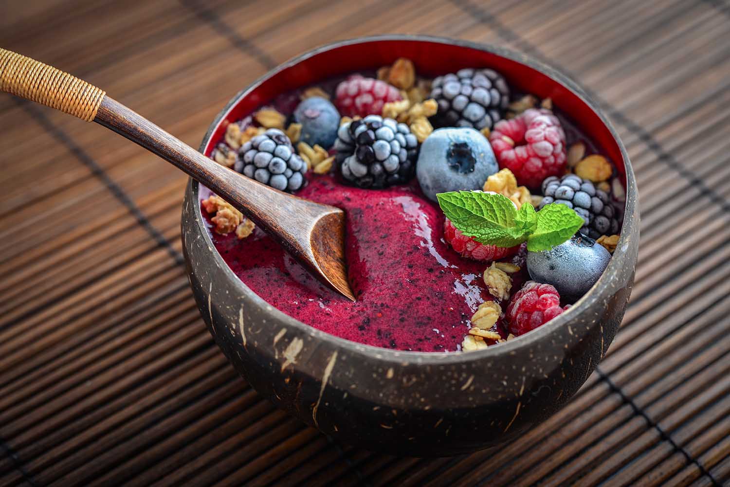 Acai smoothie bowl with blueberry, blackberry, raspberry, granola and chia seeds in bowl from coconut shell