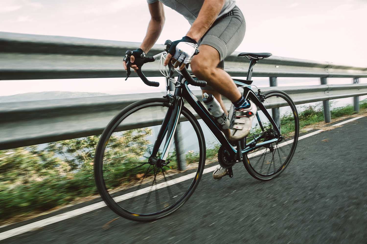 Detail of a road bike with a cyclist pedaling on a road.