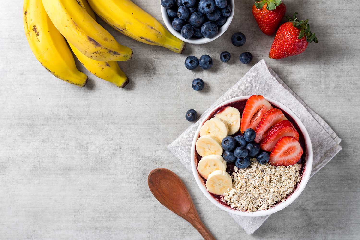 Brazilian frozen açai berry ice cream bowl with strawberries, bananas, blueberry and oatmeal flakes. with fruits on wooden background. Summer menu top view