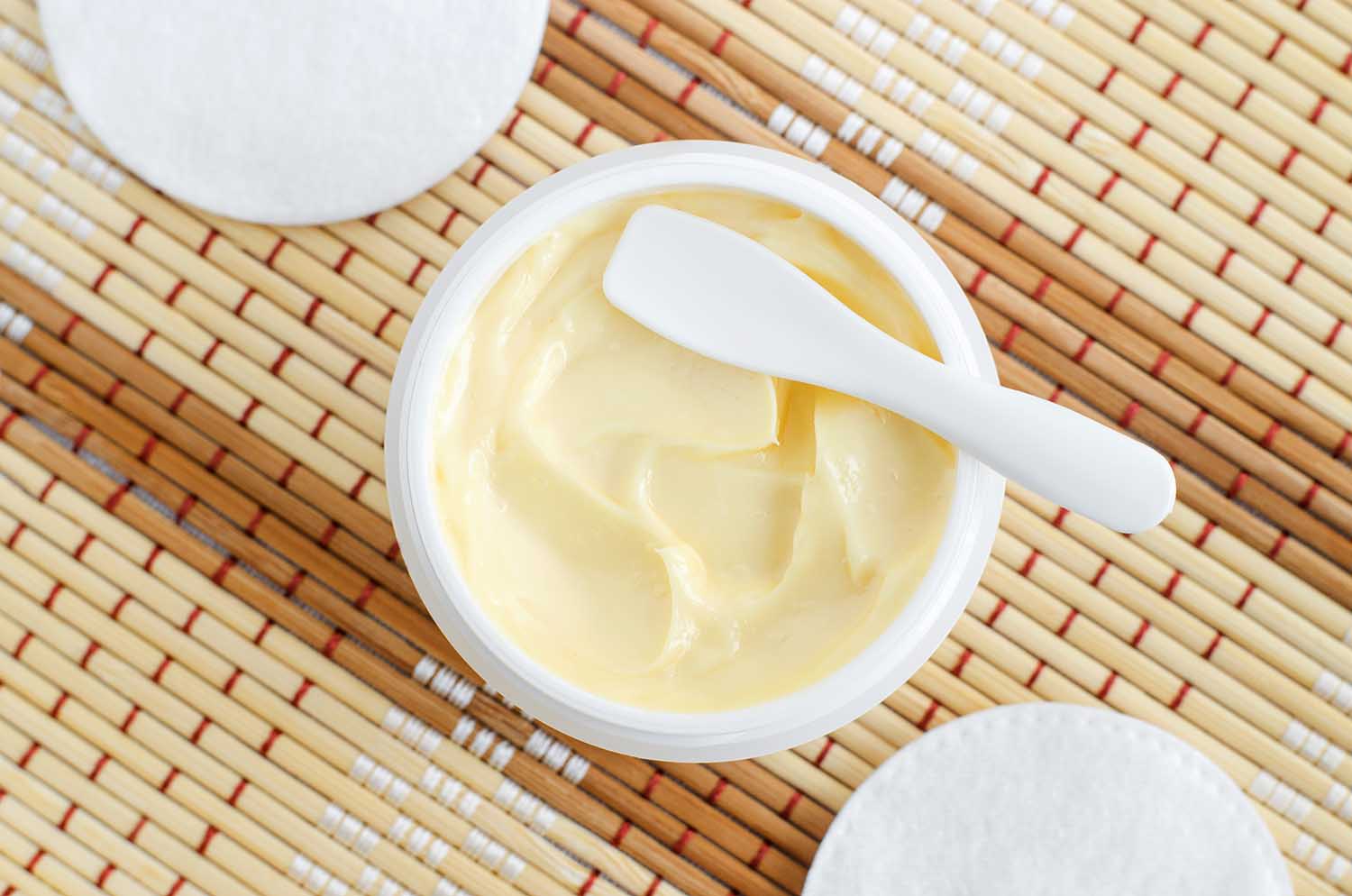 Yellow facial mask (banana face cream, shea butter hair mask, body butter) in the small white container. Natural skin and hair concept. Top view, copy space.