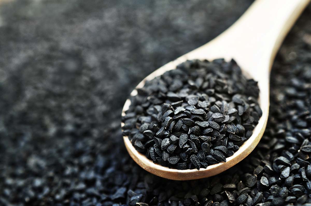 Black cumin (nigella sativa or kalonji) seeds in spoon on wooden background, selective focus, toned