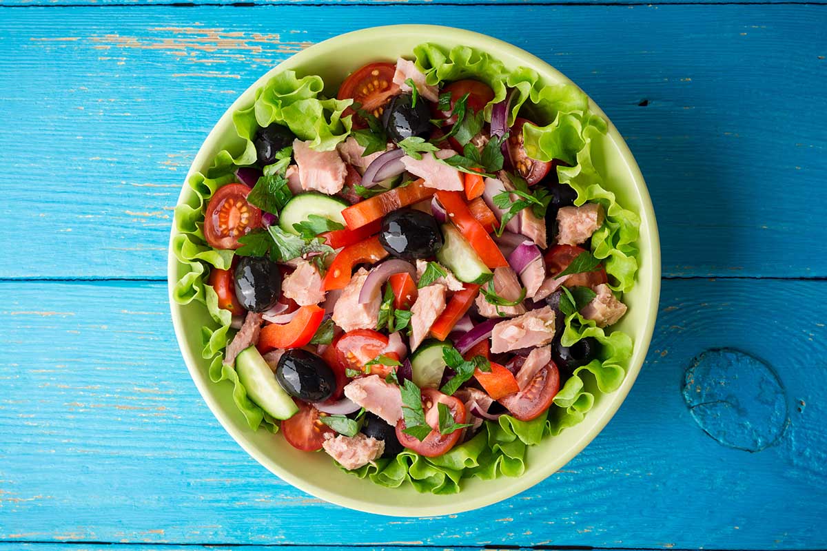 Salad with vegetables and tuna on rustic blue wooden table. Top view.