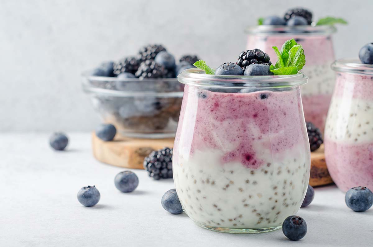 Acai berry and chia seed pudding with blueberries and blackberries in glass jars on a light white table. Copy space, horizontal image, front view