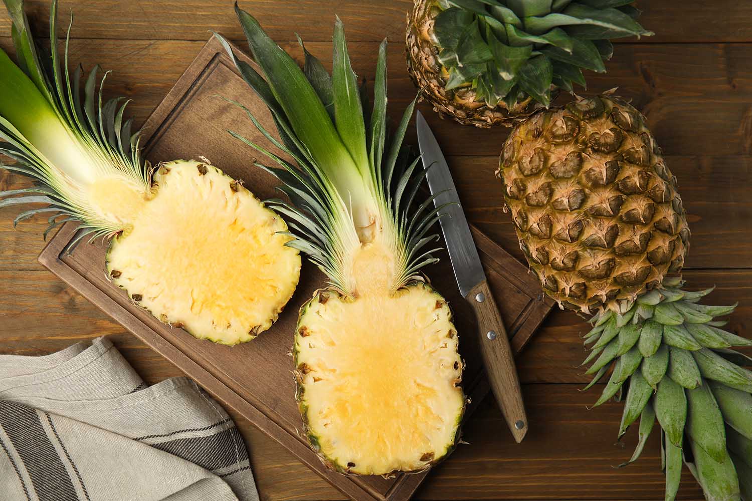 Whole and cut pineapples on wooden table, flat lay
