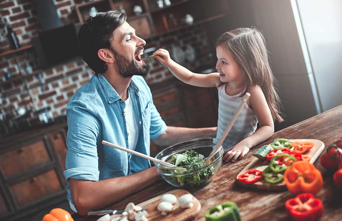 Handsome man and his little cute daughter are cooking on kitchen. Making salad. Healthy lifestyle concept.