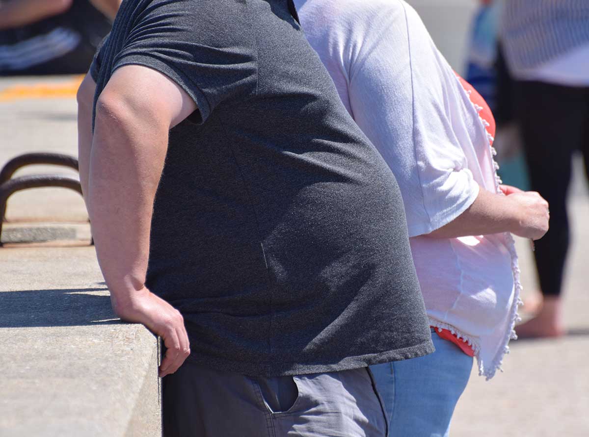 Dorset, UK. May 25 2020. An obese couple standing against a wall in the street. Research shows evidence that obesity and obesity-related conditions seem to worsen the effect of Coronavirus COVID-19.