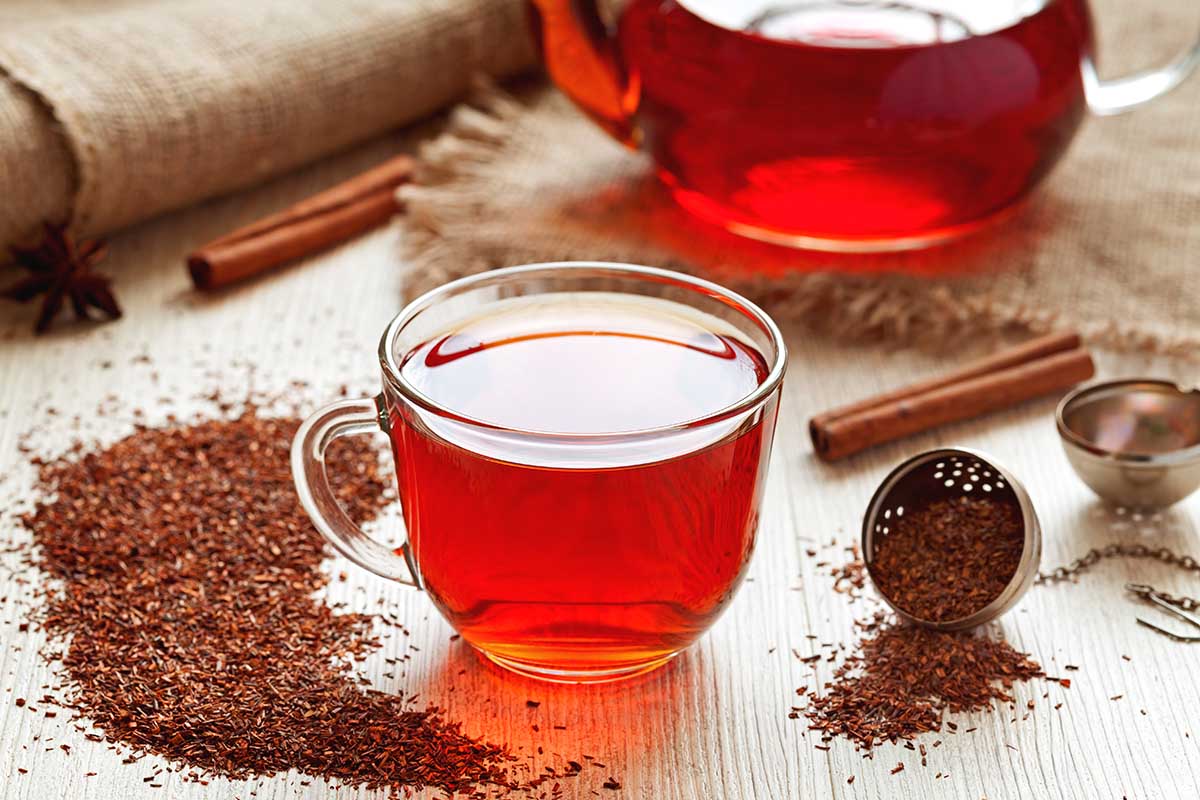 Cup of healthy traditional herbal rooibos red beverage tea with spices on vintage wooden table