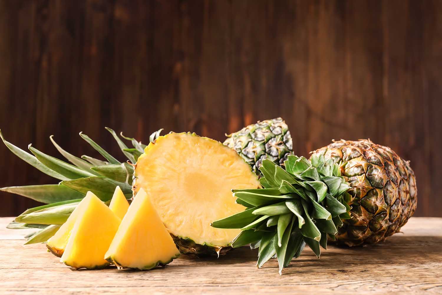 Whole and cut ripe pineapples on wooden table