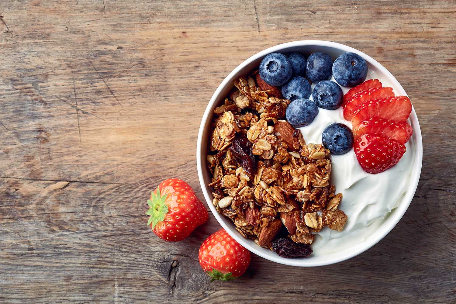 Bowl of homemade granola with yogurt and fresh berries on wooden background from top view