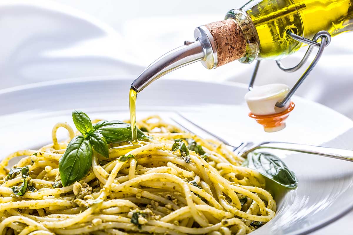 Spaghetti with homemade pesto sauce pouring olive oil and basil leaves.