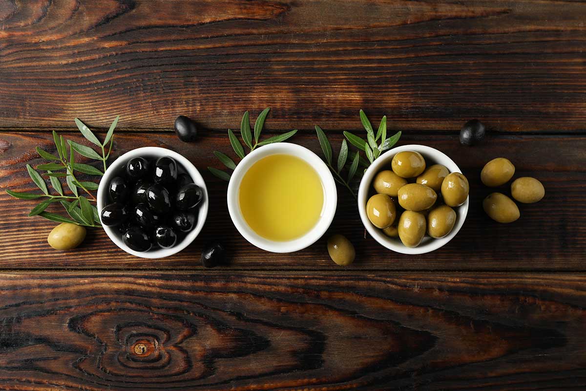 Bowls with olives and oil on wooden background, space for text
