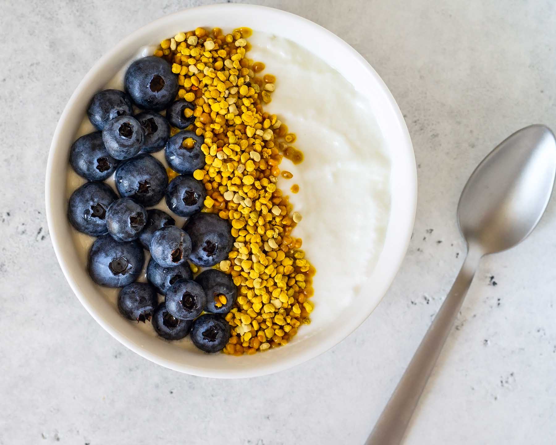 Bowl of greek yogurt, bee pollen and fresh berries on white stone background. Healthy breakfast. Top view.