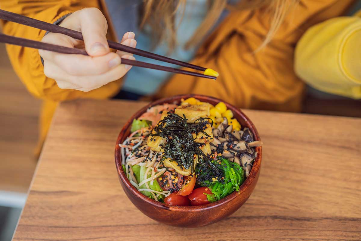 Woman eating Raw Organic Poke Bowl with Rice and Veggies close-up on the table. Top view from above horizontal